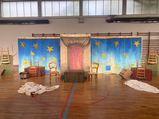 Chez Roxane Décor de scène avec 3 paneaux peints montrant une nuit étoilée devant une porte Haussmannienne et accessoires devant (Chaises, coffres).